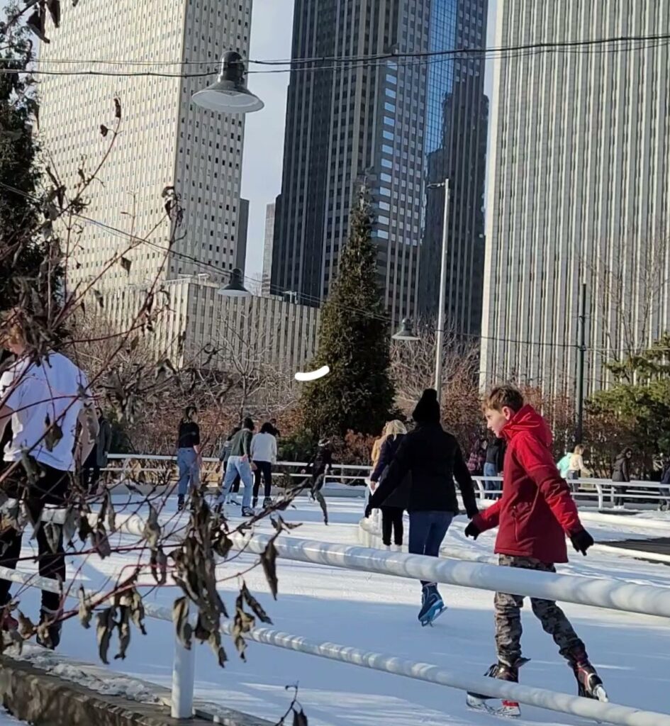 Skaters on the Maggie Daley Park ice skating ribbon in Chicago with downtown skyscrapers towering behind on a clear winter day