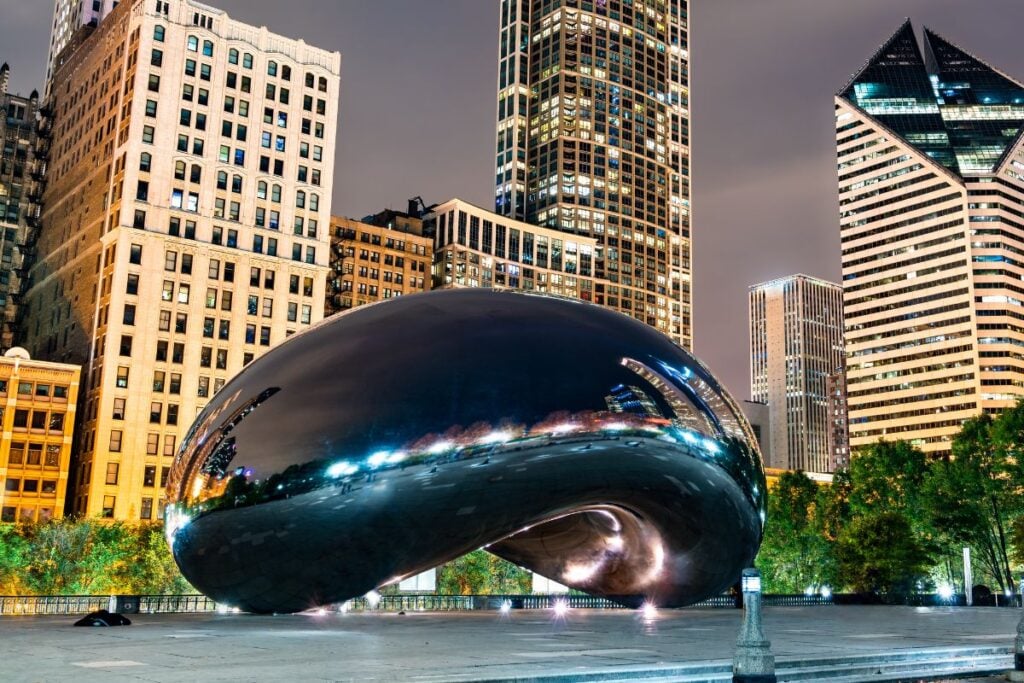 Cloud Gate sculpture in Millennium Park at night with Chicago skyline reflecting on the surface of the Bean