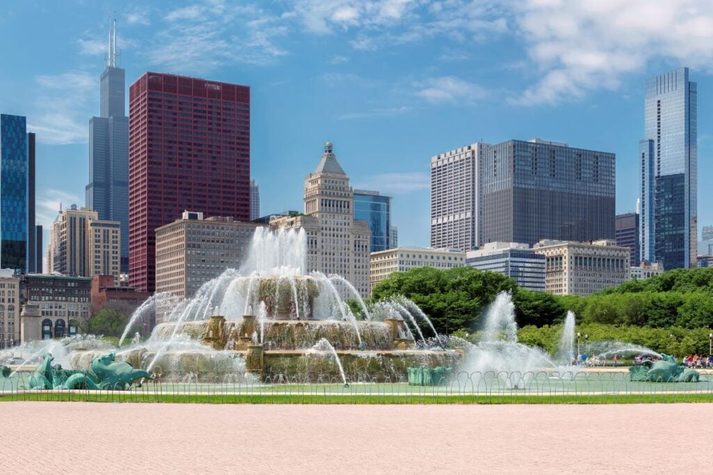 Buckingham Fountain spraying water in Grant Park with the Chicago skyline in the background on a sunny day.