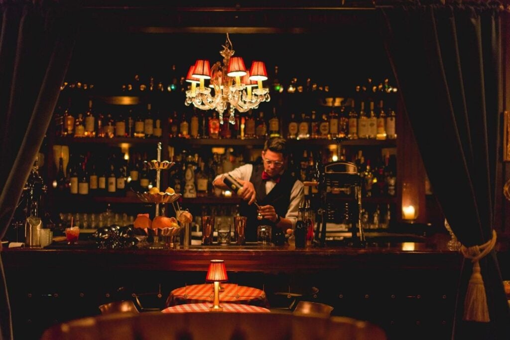 Bartender mixing a cocktail beneath a chandelier in the dimly lit, intimate dining room at Ciccio Mio in Chicago's River North