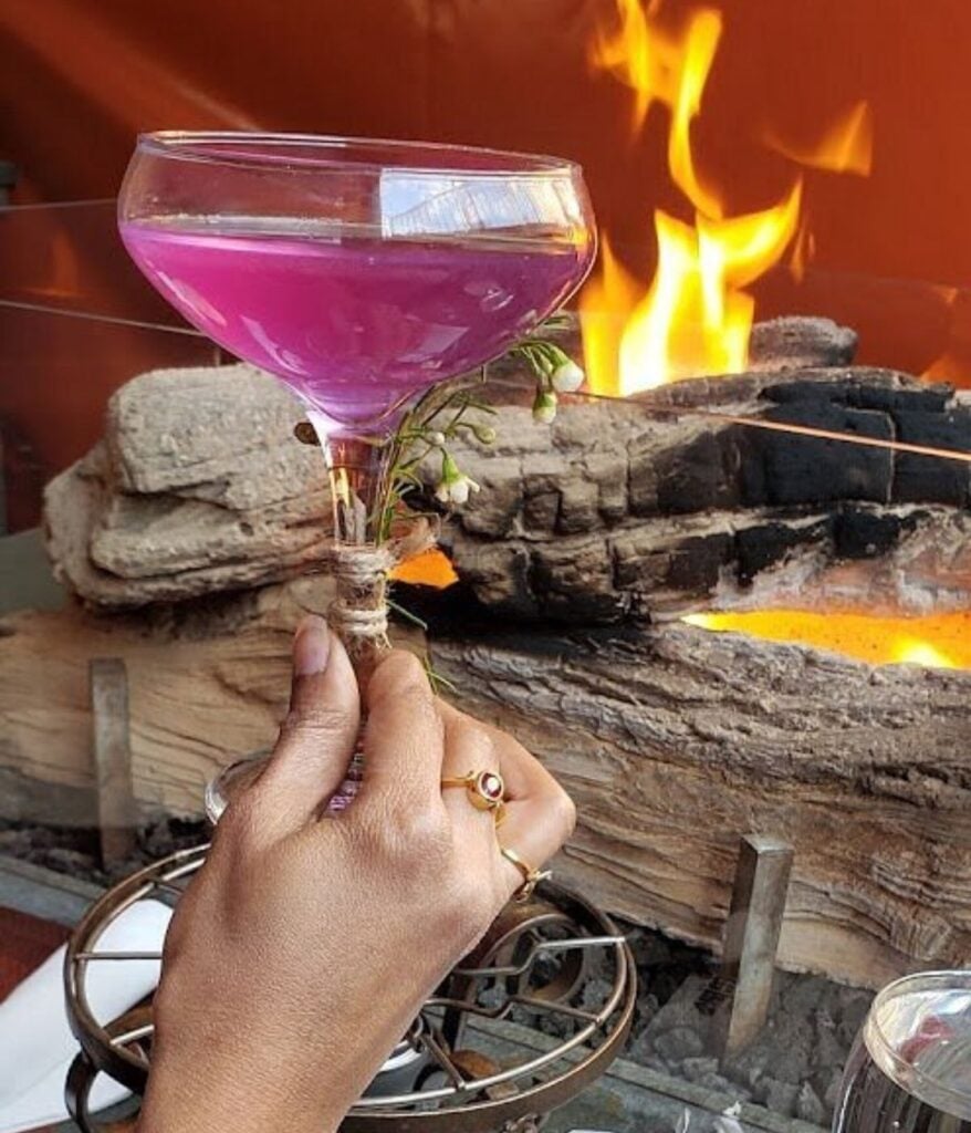 Purple cocktail garnished with white flowers held beside an open flame at Geja's Cafe in Lincoln Park, Chicago