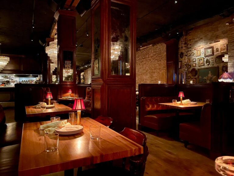 Dim, candlelit steakhouse dining room with red table lamps, leather booths, and exposed brick in Chicago