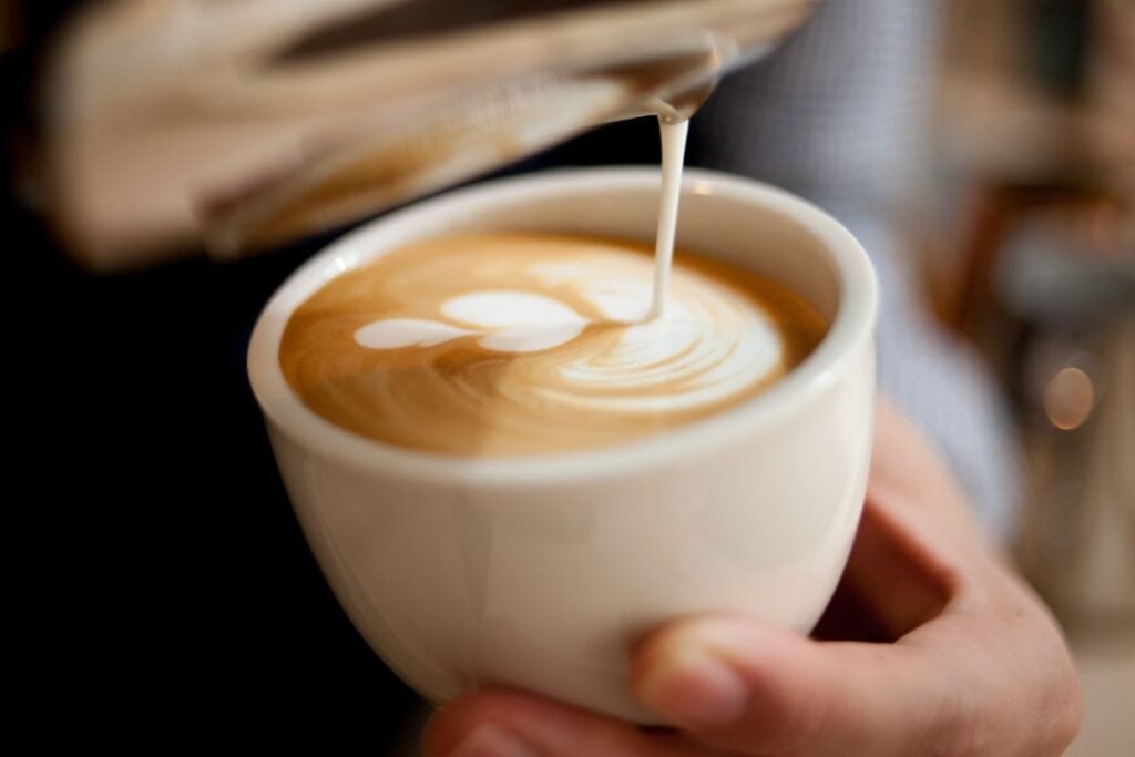 Barista pouring latte art into a white ceramic cup at a coffee shop