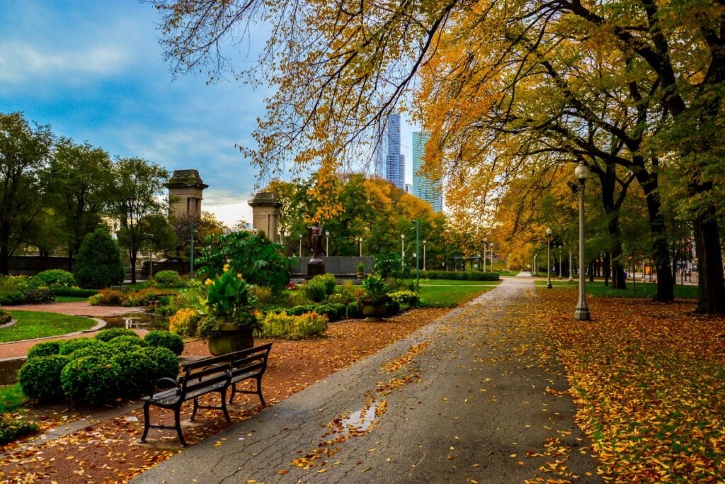Leaf-covered path and bench in Grant Park Chicago with autumn trees and the skyline behind