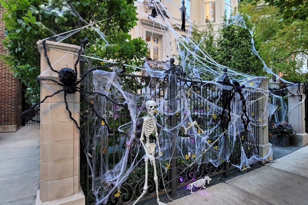Giant spiders, a skeleton, and fake cobwebs covering the iron gate of a Chicago home for Halloween