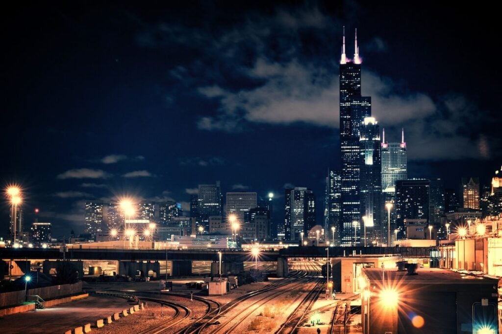Chicago skyline at night with Willis Tower lit up above rail lines and glowing streetlights