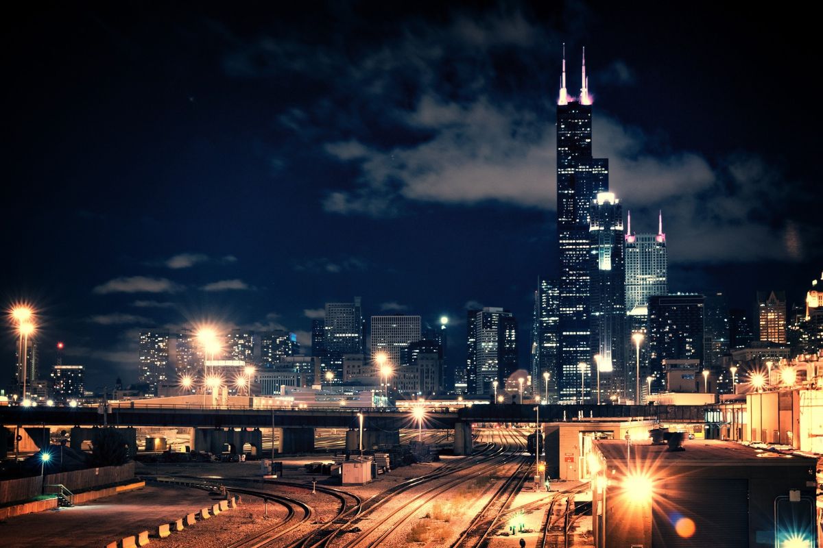 Chicago skyline at night with Willis Tower lit up above rail lines and glowing streetlights